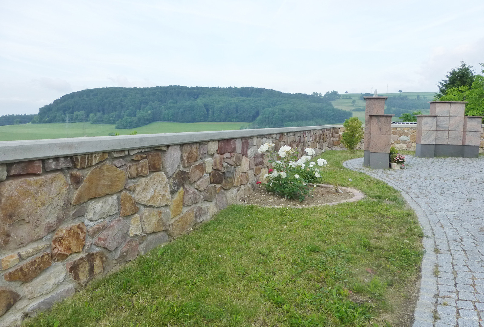 Natursteinmauer mit Weitblick ins Tal, Rosenbeet und Steinstelen