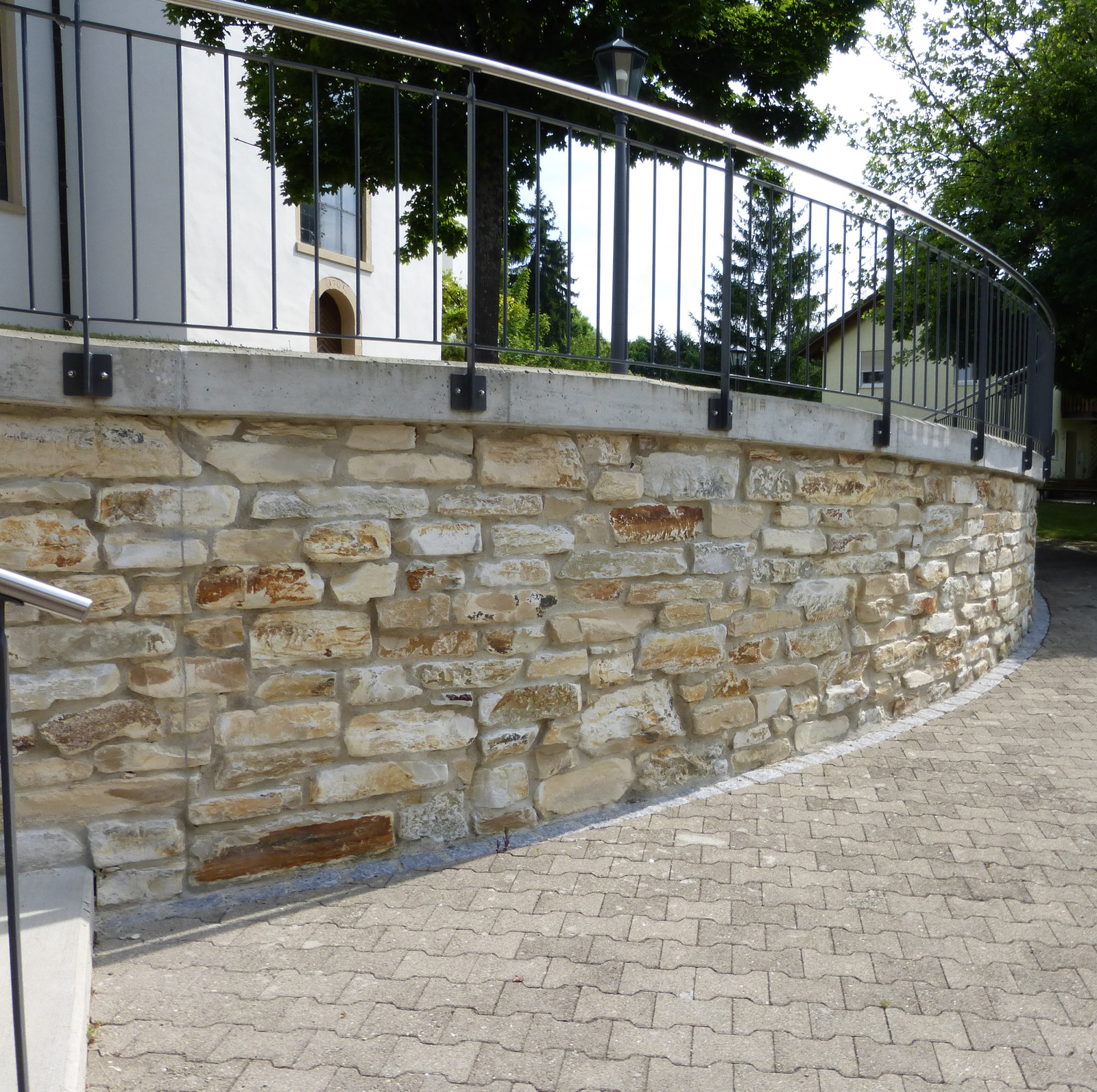 Geschwungene Natursteinmauer mit Geländer
