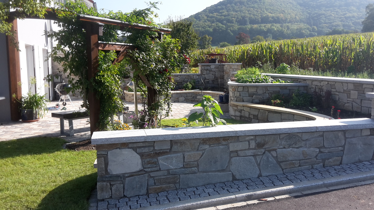 Natursteinmauer mit Pergola und Hochbeeten am Feldrand